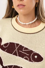 Sweater color manteca de tejido de punto con cuello redondo y ribete marrón. Presenta dos peces marrones tejidos en el frente con detalles bordados a mano.