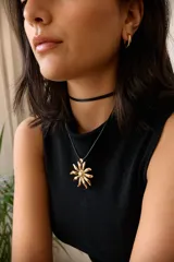 Collar con tiento negro y dije plateado en forma de flor con centro texturizado.