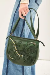 Cartera bandolera verde de cuero vacuno con bordado de flores y tachas doradas y plateadas. Tiene cierre metálico superior, forro de algodón, división interna, bolsillo y tarjetero. La correa es regulable.