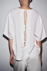 Top de lino color blanco, con cuello redondo y mangas cortas. Detalle de abertura en la espalda ajustable con lazadas.