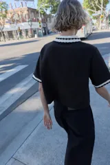 Top de tejido negro con cuello polo y bordes de manga cortos con diseño de ondas en blanco y negro. Tiene un cierre frontal de botones.