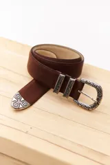 Cinturón marrón de cuero con hebilla metálica plateada con diseño floral.