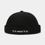 Gorro estilo docker color negro con la frase 'it is what it is.' bordada en blanco.