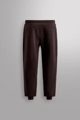 Pantalón jogger color marrón oscuro, corte regular fit, confeccionado en tejido técnico compacto de algodón con elasticidad. Cuenta con cintura elástica ajustable con cordón, bolsillos frontales y bolsillo lateral con cierre de cremallera.