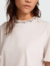 Remera de algodón color blanco roto, de corte holgado y manga corta con bordes deshilachados. Presenta un cuello redondo adornado con cristales cabujón engarzados.