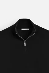 Jersey negro de punto de algodón, corte recto, cuello perkins con cremallera metálica y mangas largas terminadas en rib.