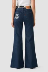 Jeans acampanados de tiro alto, color azul oscuro, con pretina y bolsillos delanteros con estampado de vaca en blanco y negro.