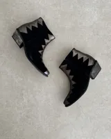 Botín de cuero vacuno negro con detalles de cuero plateado en forma de zigzag en el borde superior y en la puntera.
