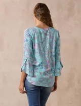 Blusa de seda fría estampada con flores en tonos celeste, lila y verde. Tiene cuello redondo con escote en V entrelazado y mangas 3/4 acampanadas.