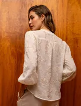 Blusa color crema de gasa bordada, con escote en V, abertura central con botones y mangas largas con puño.