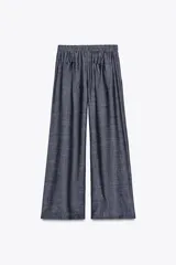 Pantalón ancho azul con textura de lino, tiro alto, cintura elástica con cordón ajustable, pinzas delanteras, bolsillos laterales y traseros, y cinturón de la misma tela con apliques metálicos.