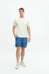 Short de baño largo azul con estampado abstracto de hojas en tonos azules más claros. Posee cintura elástica con cordón de ajuste gris, bolsillos laterales y un bolsillo trasero.