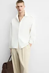 Camisa de algodón color blanco hueso, de corte relajado (relaxed fit), con cuello solapa y manga larga terminada en puño con botón. Cierre frontal con botonadura.