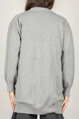 Cardigan oversize negro con escote en V, cierre frontal de botones y broches decorativos con perlas en el lado izquierdo.