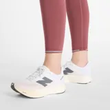 Calza deportiva New Balance color ladrillo, de tiro alto, con bolsillos laterales y detalles reflectivos en el ruedo.