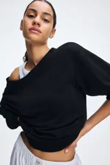 Buzo negro con escote off-the-shoulder, hombros caídos, corte holgado y mangas largas con puños acanalados.