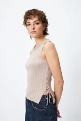 Musculosa de punto color beige, con textura acanalada y detalle de trenzado lateral ajustable.