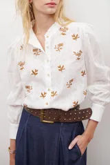 Camisa azul marino con estampado floral en color lila, cuello mao con volantes, cierre frontal de botones y mangas largas abullonadas con puños elásticos.