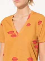Remera color mostaza de punto flamé con estampado de labios rojos, escote en V profundo, mangas cortas y corte a la altura de la primera cadera.