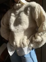 Sweater tejido de lana merino color crudo, con cuello alto y mangas largas abullonadas. Tejido artesanal con punto grueso.