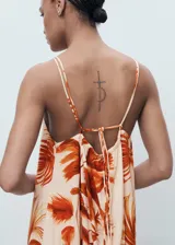 Vestido largo de viscosa con estampado de palmeras en tonos naranjas y terracota sobre fondo beige claro. Presenta tirantes finos ajustables y un detalle fruncido en el escote.