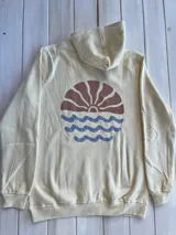 Hoodie color crema con estampado en la espalda de un sol naciente sobre el mar.