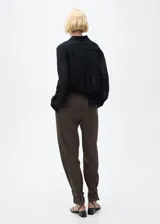 Pantalón wideleg color marrón, de tejido fluido y tiro medio. Presenta trabillas, cierre delantero con cremallera, gancho y doble botón, detalle de pinzas, dos bolsillos laterales, diseño largo, forro interior y bajo abotonado.