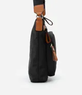 Bandolera negra de poliéster con detalles en cuero sintético color marrón. Tiene correa transversal ajustable, cierre de cremallera, bolsillos delanteros y placa metálica con el logo de la marca.