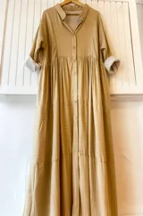 Vestido camisero largo color beige con rayas verticales blancas, cuello camisero, mangas largas con puños con dobladillo y falda escalonada con volados.