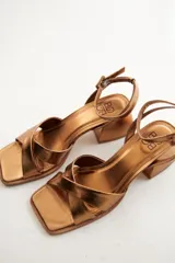 Sandalias plateadas de cuero, con tiras cruzadas sobre el empeine, pulsera al tobillo con hebilla y taco bajo cuadrado.