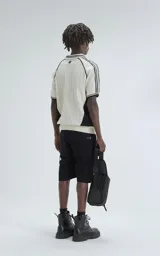 Chomba tejida de hilo color crudo con detalles en negro, de corte recto y manga corta. Presenta cuello tipo polo con rayas y bordado con el número 90 y la palabra 'Ravers'.