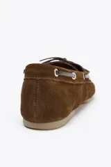 Zapato náutico color marrón de serraje con detalle de pespuntes en el cuerpo y pasados en los laterales. Cierre mediante cordones y suela efecto engomado.