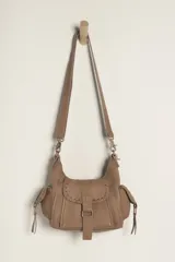 Bolso mini de cuero desgastado color topo, con cierre magnético plegable, monedero forrado y correa de hombro ajustable. Presenta detalles de tachas y costuras decorativas en el fuelle frontal.