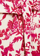 Mono largo de viscosa color crema con estampado floral fucsia, cuello camisero, manga corta, dos bolsillos laterales, trabillas y cinturón con lazo.