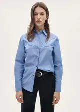 Camisa celeste de manga larga con puños abotonados, diseño recto, cierre delantero de botones a presión, cuello camisero, costuras decorativas, tachuelas decorativas y bordado decorativo.