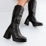 Bota alta de cuero vacuno color negro, con taco de madera forrado en cuero de 7cm, entre suela de goma de 2cm forrada en cuero, inclinación de horma de 5cm, altura de caña de 36cm, cierre YKK del lado interno y pequeño elástico en la parte superior de la caña del lado interno.