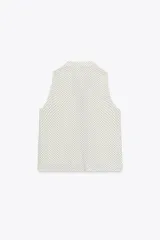 Camisa blanca con lunares negros, cuello redondo y escote pico. Sin mangas, con detalle de ribete negro en el escote y cierre frontal con botones.