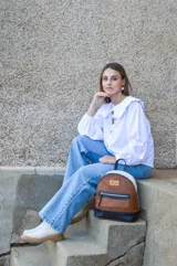 Mochila de cuero color tostado, con base y espalda en negro y tapa superior en blanco. Tiene un bolsillo frontal con cierre y un pequeño aplique de cuero con el logo de la marca.