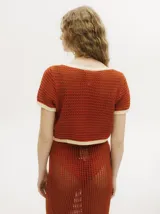 Top tejido calado color azul petróleo con cuello en V y botones carey. Tiene mangas cortas y puños en color amarillo contrastante.