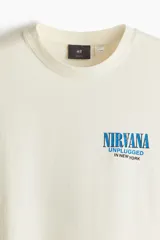 Remera color crema de corte holgado con cuello redondo y estampado frontal con el logo de la banda Nirvana y la frase 'Unplugged in New York' en color azul.