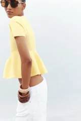 Chaqueta color amarillo claro de tejido de punto, con cuello redondo, manga corta, corte peplum y cierre frontal con botones.