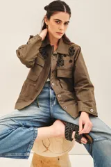 Campera color verde militar con bordados de piedras negras en el canesú delantero y trasero. Tiene bolsillos con solapa en el pecho, jareta ajustable en la cintura y cierre frontal con botones.