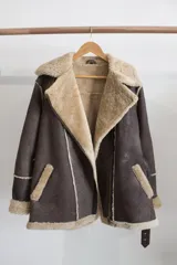 Campera gamulán marrón con interior de piel sintética color beige, cierre cruzado con cremallera y cuello con solapas amplias.
