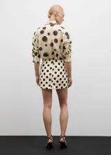 Minifalda color crema con estampado de lunares negros, corte recto y cierre trasero invisible.