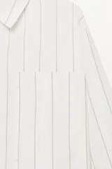 Camisa tipo pijamera de algodón a rayas verticales grises sobre fondo blanco, con cuello solapa, manga larga, bolsillos de plastrón y cierre frontal con botones.