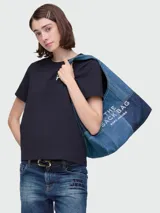 Bolso tipo saco (sack bag) de mezclilla (denim) con diseño patchwork en tonos de azul. Presenta texto estampado en blanco en el lateral: "THE SACK BAG MARC JACOBS".