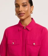 Camisa color beige de tela airflow, con cuello camisero, mangas cortas con detalle de pliegue, bolsillos con solapa en el pecho y cierre frontal con botones metalizados.