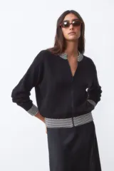 Campera bomber negra de tejido de punto con cuello, puños y ruedo acanalados con rayas blancas.