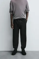 Pantalón jogger negro de corte slim fit, confeccionado en tejido de algodón con cintura elástica ajustable con cordón, bolsillos frontales y traseros de vivo, y bajo con puño elástico.