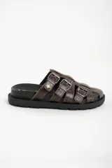 Zueco tipo pescador de cuero marrón con textura cocodrilo. Presenta tres tiras ajustables con hebillas metálicas plateadas sobre el empeine. Tiene una suela negra gruesa y dentada.